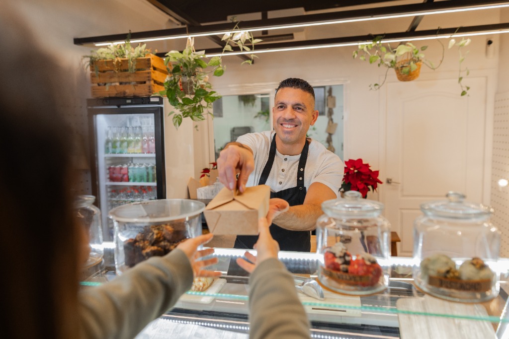 Artesana de panadería entregando con una sonrisa un pedido para llevar en el mostrador.